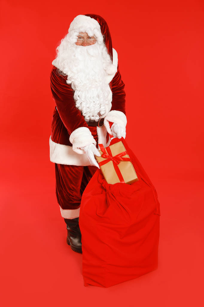 Autentický Santa Claus s pytlem a dárkem na červeném pozadí - Fotografie, Obrázek