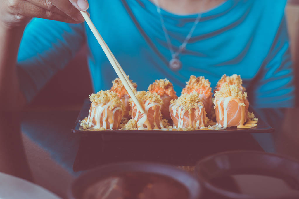 Руки с палочками для еды с сыром суши на блюде и японским соусом шою в ресторане
 - Фото, изображение
