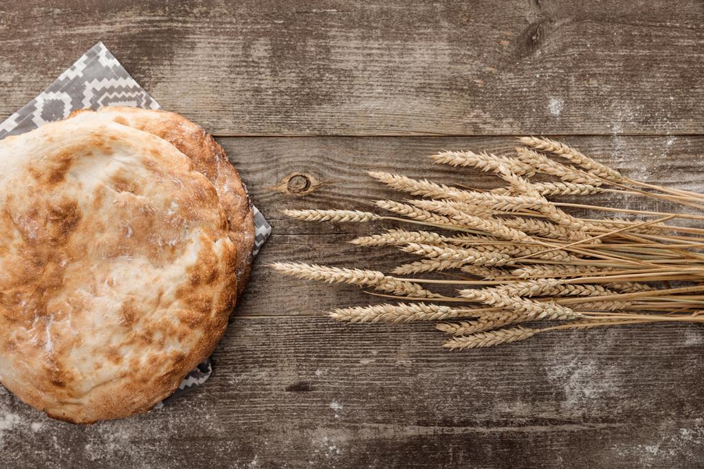 vista superior do pão de lavash na toalha cinza com padrão perto de picos de trigo na mesa de madeira
 - Foto, Imagem