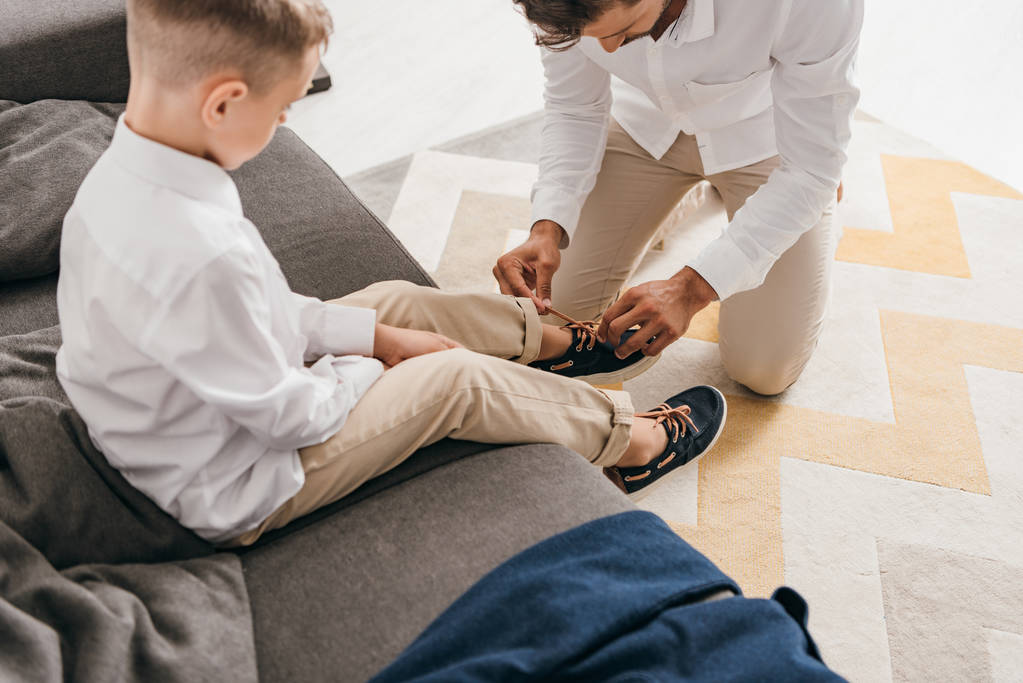 自宅で息子のために靴ひもを結ぶ父親のトリミングされたビュー - 写真・画像