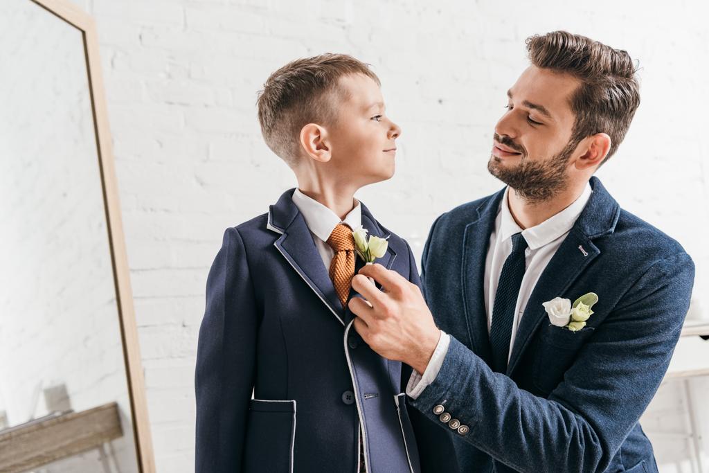 smiling dad and son in jackets with boutonnieres looking at each other - Photo, Image