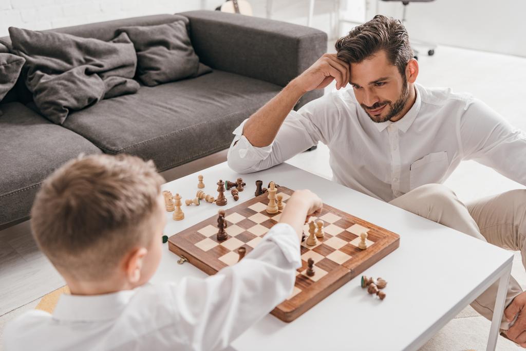 Ο μπαμπάς και ο γιος παίζουν σκάκι μαζί στο σπίτι. - Φωτογραφία, εικόνα