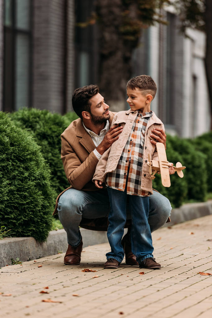 parrakas isä ja hymyilevä poika lelukone katselee toisiaan kadulla
 - Valokuva, kuva
