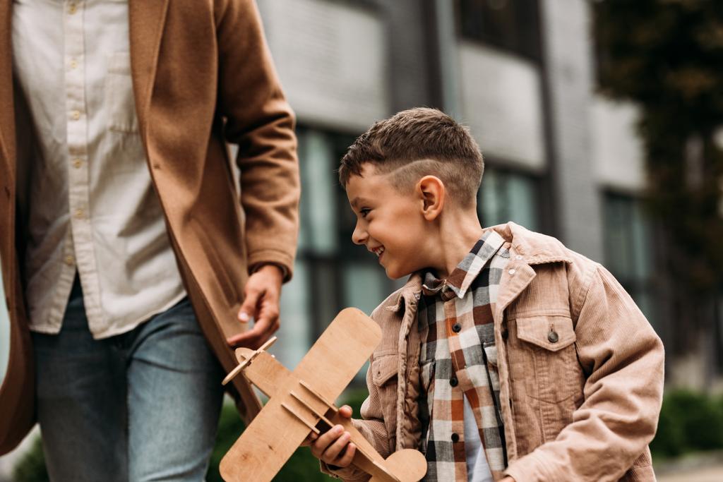 Teilansicht von Papa im Mantel und lächelndem Jungen, der mit Holzspielzeug auf der Straße spielt - Foto, Bild