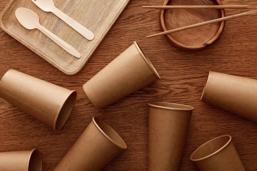 vista superior de platos de madera, cubiertos, palillos y vasos de papel sobre fondo marrón
 - Foto, Imagen