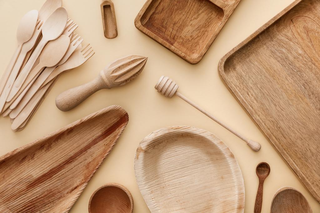 Widok z góry na drewniane płyty, naczynia, widelce, łyżki i Wyciskarka do rąk na beżowym tle - Zdjęcie, obraz