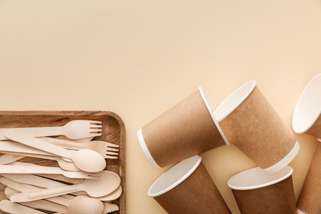 top view of rectangular wooden dish with forks and spoons near paper cups on beige background - Photo, Image
