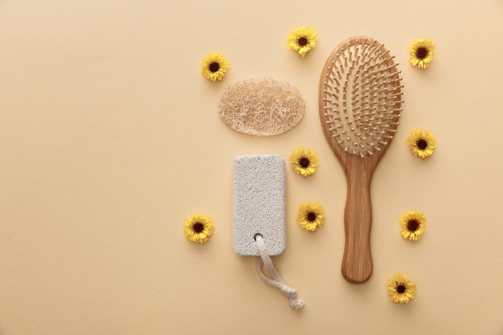 vista superior de escova de cabelo de madeira, pedra-pomes e loofah no fundo bege com flores
 - Foto, Imagem