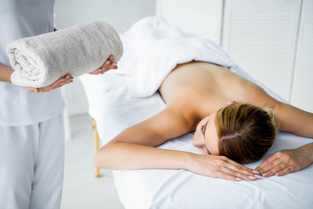 vista recortada de masajista sosteniendo toalla y mujer acostada en alfombra de masaje
  - Foto, imagen