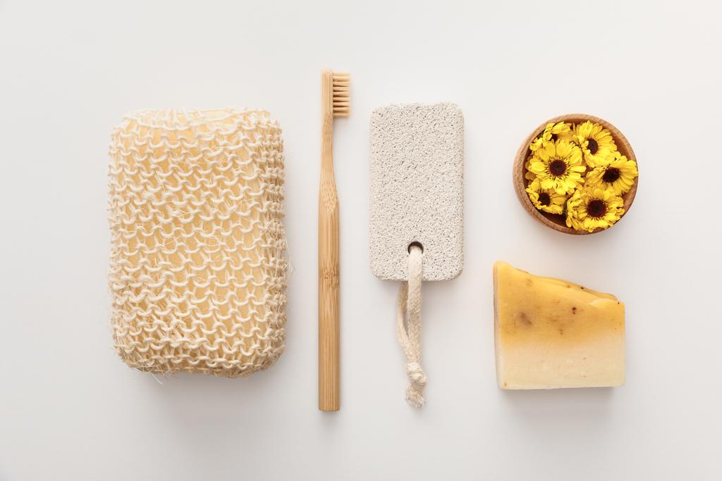 acostado plano con esponja de baño cerca del cepillo de dientes, pedazo de jabón, piedra pómez y taza con flores sobre fondo blanco
 - Foto, Imagen