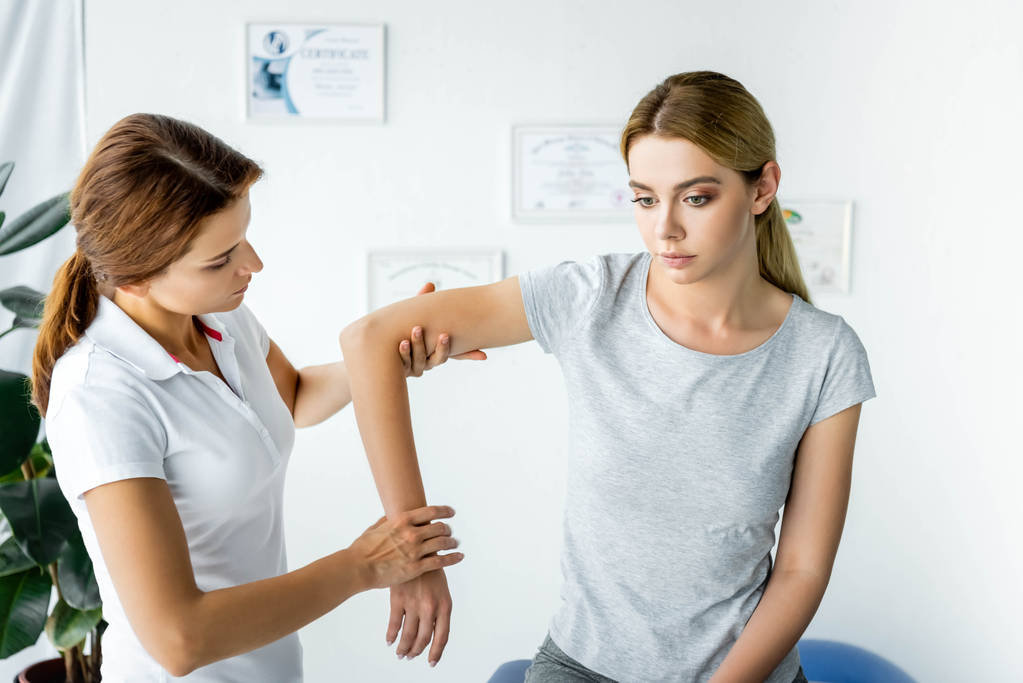 kiropraktikko koskettaa houkuttelevan potilaan kättä harmaassa t-paidassa
  - Valokuva, kuva