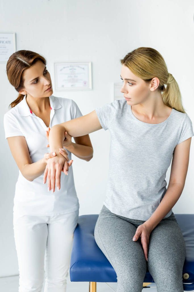 chiropractor touching hand of attractive patient in grey t-shirt  - Photo, Image