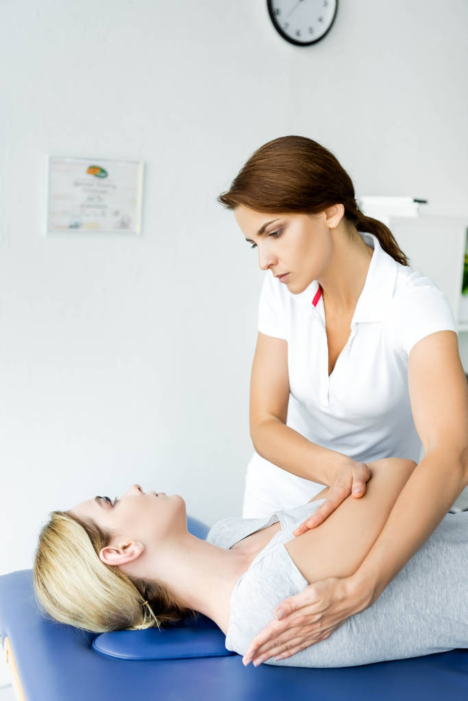 хіропрактик торкається руки пацієнта в сірій футболці в клініці
  - Фото, зображення