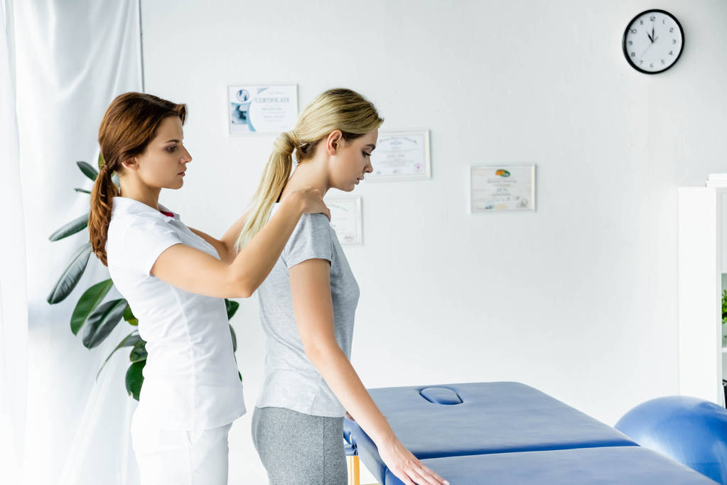 Chiropraktiker berührt Schultern attraktiver Patientin im grauen T-Shirt  - Foto, Bild