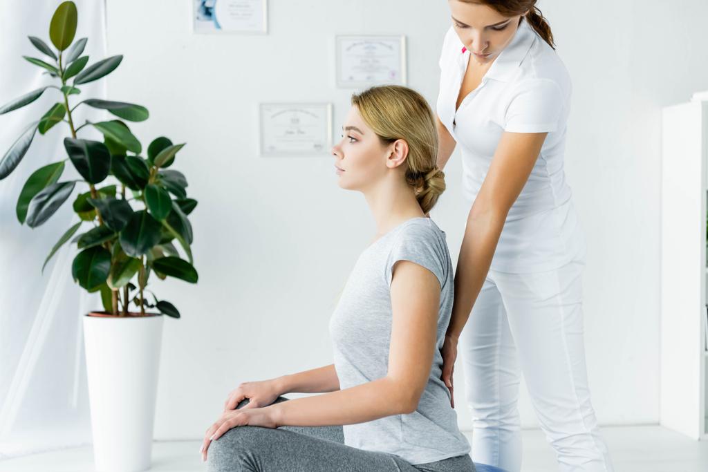 vista laterale di attraente paziente seduta e chiropratico toccandole la schiena
  - Foto, immagini