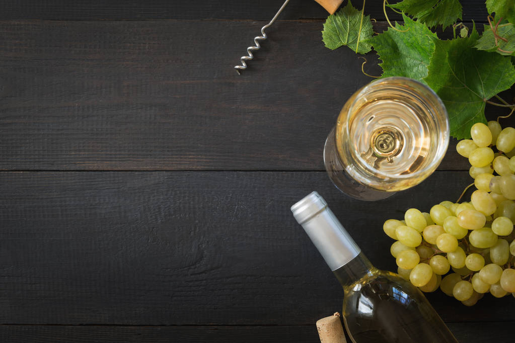 Botella de vino blanco con copa de vino, uva madura sobre mesa de madera negra
. - Foto, imagen
