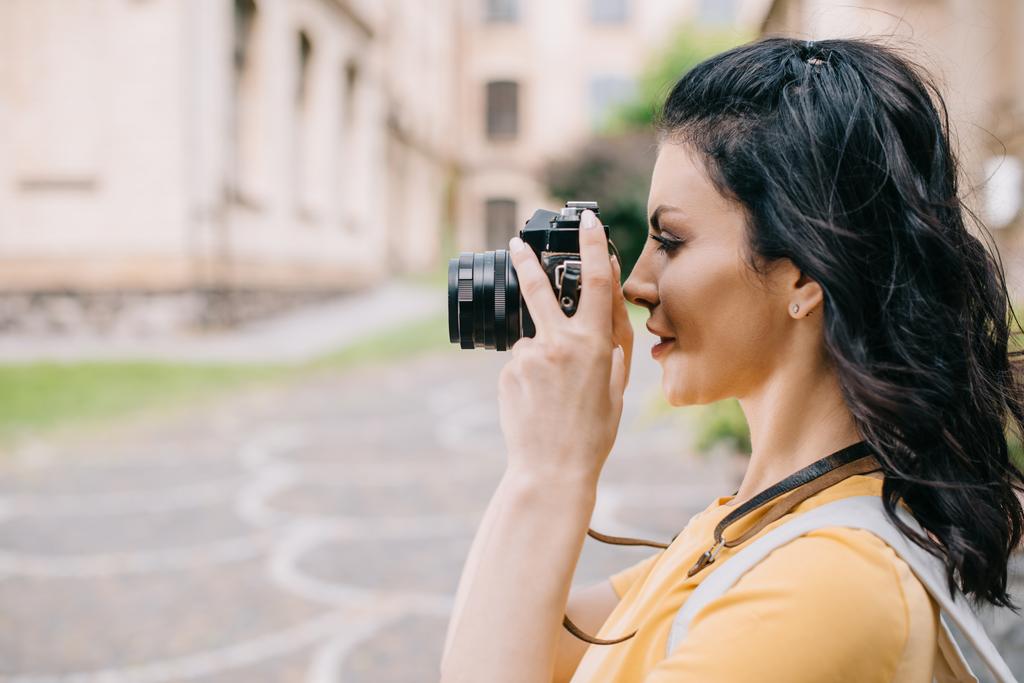 vista lateral de chica atractiva sosteniendo la cámara digital mientras toma la foto
  - Foto, imagen