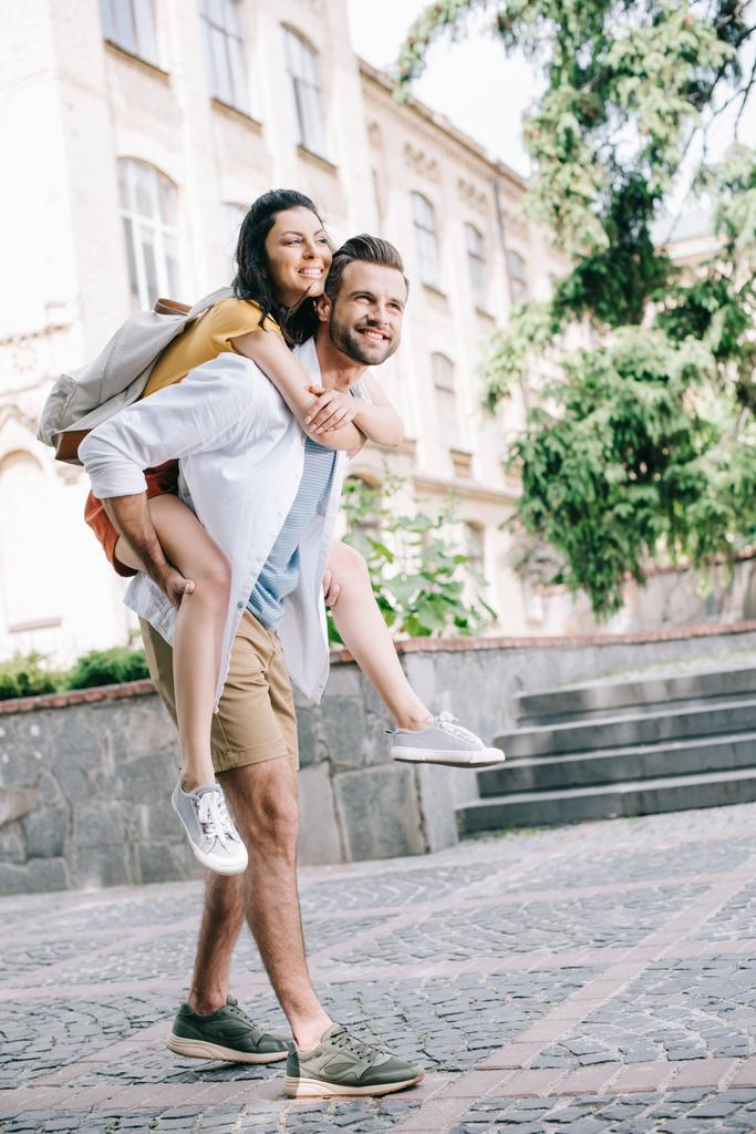 boldog szakállas férfi piggyback vidám lány közel épület  - Fotó, kép
