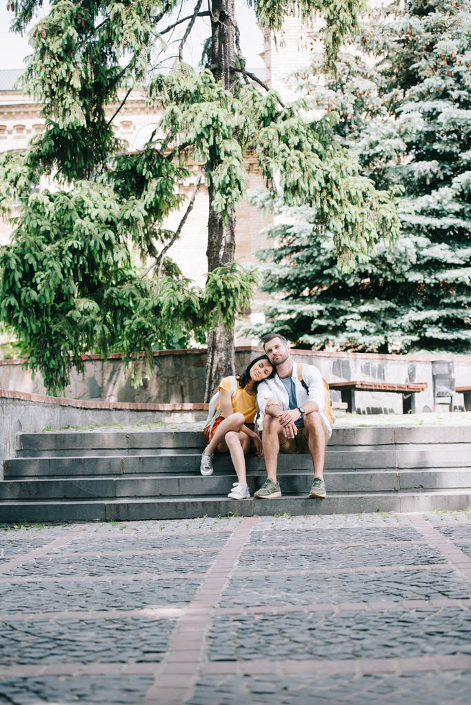 appy man en lachende vrouw zitten op de trap in de buurt van rugzakken  - Foto, afbeelding