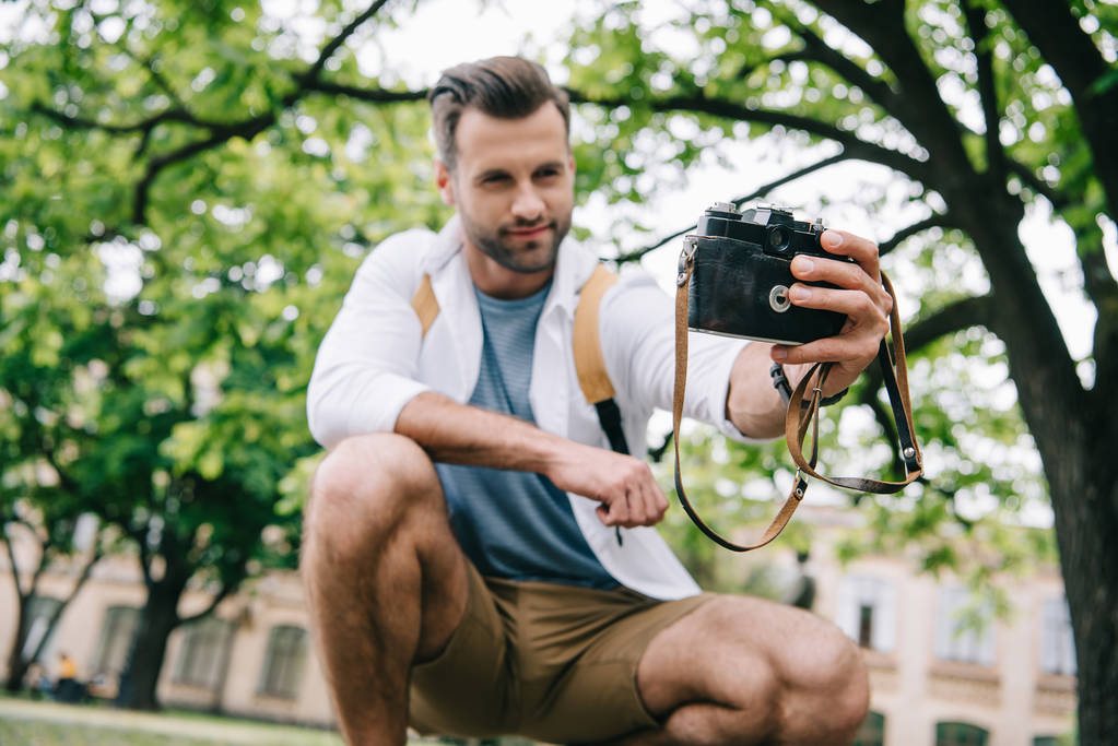 Tiefansicht eines glücklichen bärtigen Mannes, der ein Selfie mit einer Digitalkamera in der Nähe eines Gebäudes macht   - Foto, Bild