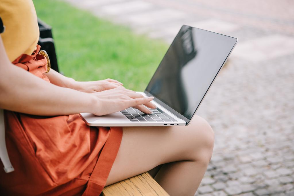 vista ritagliata di ragazza seduta su panchina e utilizzando il computer portatile con schermo bianco
  - Foto, immagini