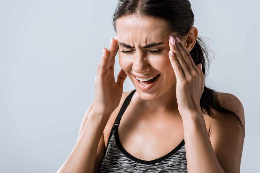 attraktive Sportlerin mit Kopfschmerzen an den Schläfen isoliert auf grau - Foto, Bild