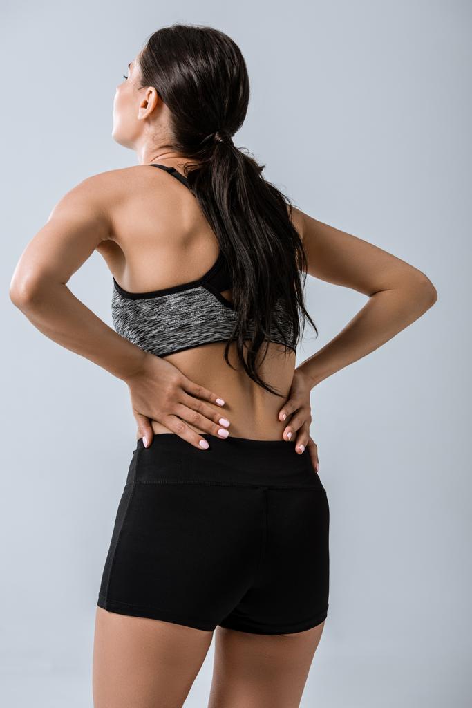 Вид сзади женщины с болями в пояснице, изолированной на сером фоне
 - Фото, изображение