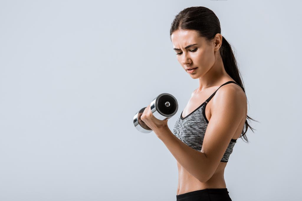attractive brunette sportswoman using dumbbell isolated on grey - Photo, Image