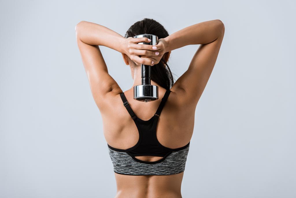 back view of brunette sportswoman using dumbbell isolated on grey - Photo, Image
