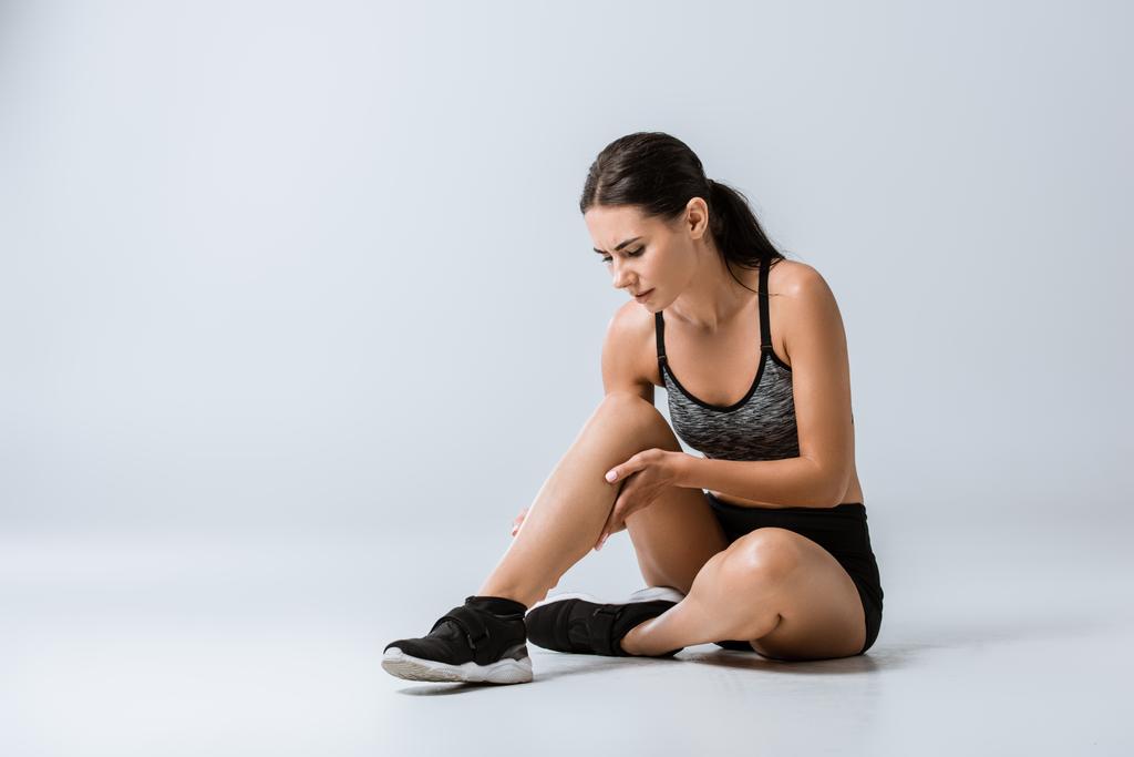 aantrekkelijke brunette Sportvrouw met been pijn op grijs - Foto, afbeelding