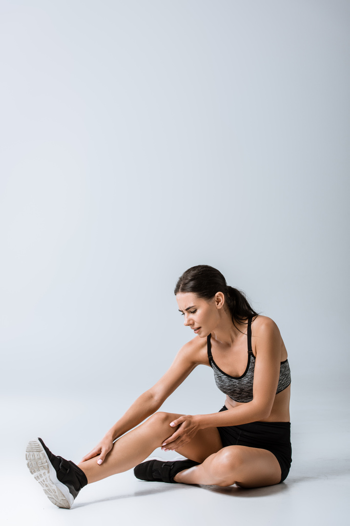 přitažlivá brunetka s bolestí nohou na šedé - Fotografie, Obrázek