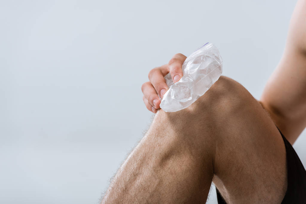 частичный вид спортсмена, использующего лед для колена, изолированного на сером
 - Фото, изображение