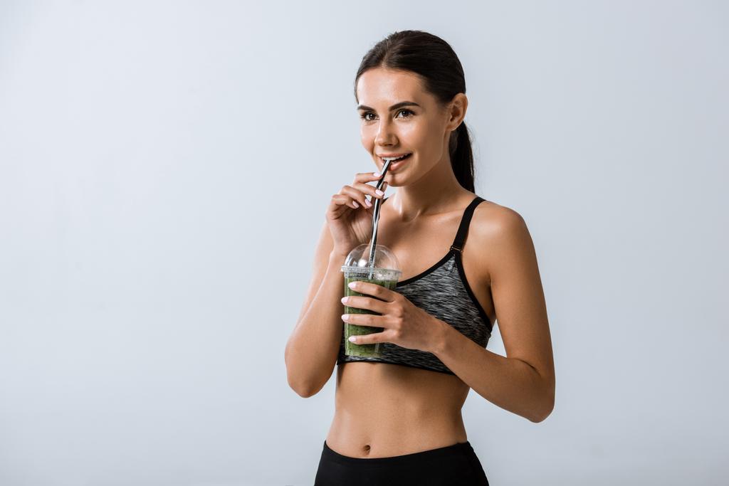 aantrekkelijke lachende Sportvrouw drinken smoothie geïsoleerd op grijs - Foto, afbeelding