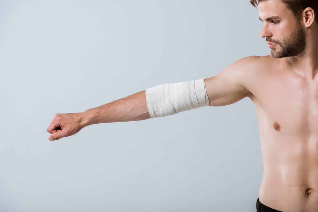Teilansicht des hemdlosen Sportlers mit elastischem Verband am Ellbogen isoliert auf grau - Foto, Bild