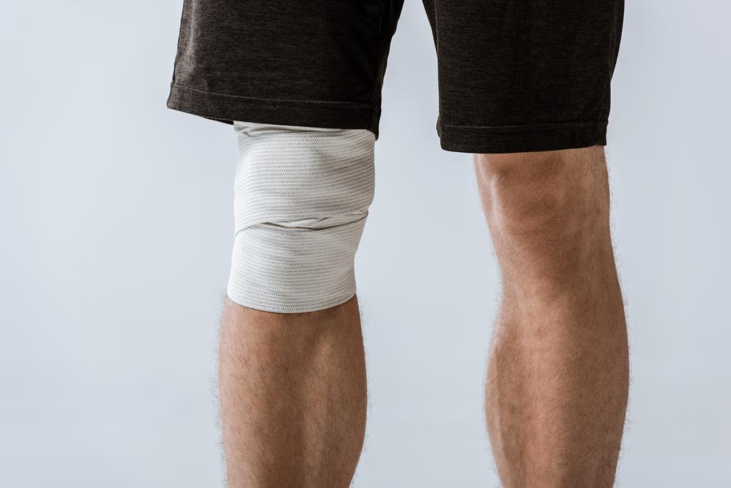 wykadrowany widok sportowca z elastyczną bandaż na kolanie na szarym - Zdjęcie, obraz