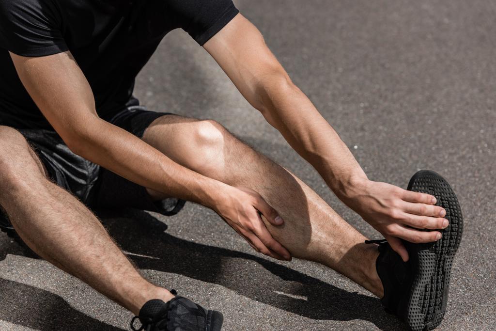 cropped view of sportsman with leg injury on street - Photo, Image
