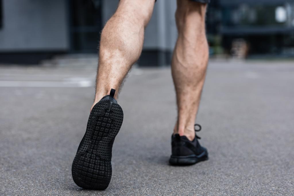 частичный вид спортсмена в черных кроссовках идущего по улице
 - Фото, изображение