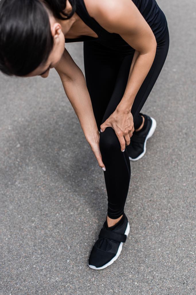 cropped view of sportswoman in black sneakers with knee pain on street - Photo, Image