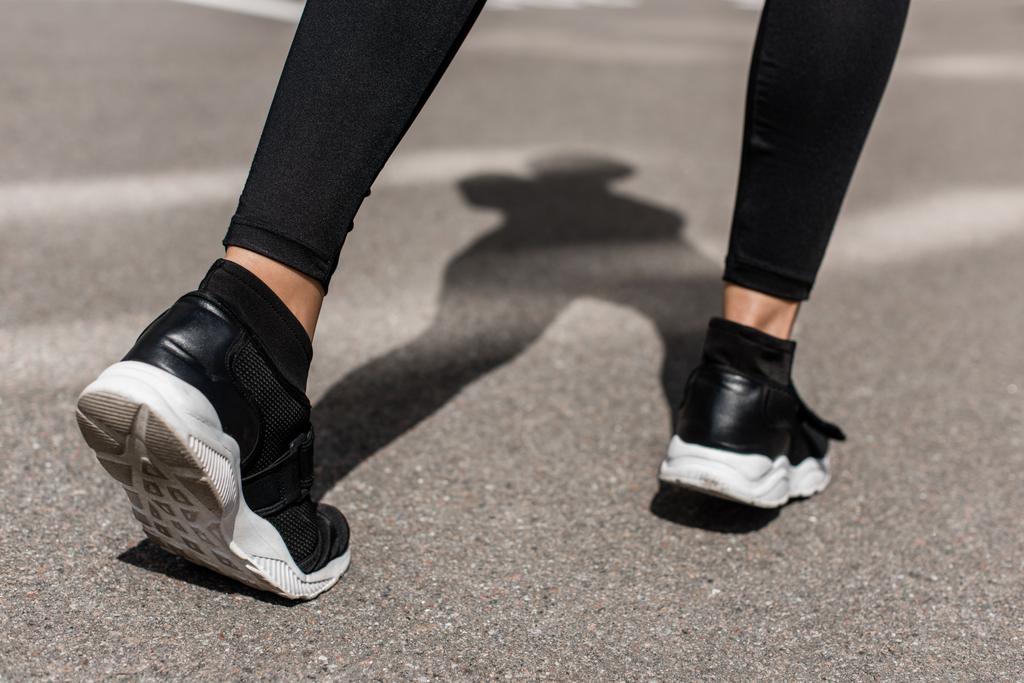 περικομμένη θέα της αθλητικής γυναίκας σε μαύρα αθλητικά παπούτσια στο δρόμο - Φωτογραφία, εικόνα
