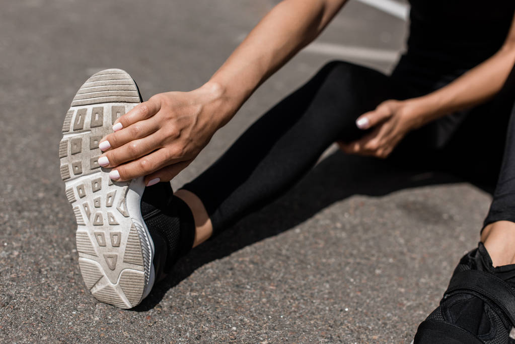 részleges kilátás sportoló lábát fájdalom nyújtás az utcán - Fotó, kép