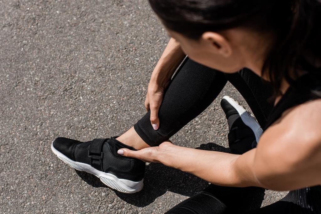 cropped view of sportswoman in black sneakers with ankle pain on street - Photo, Image