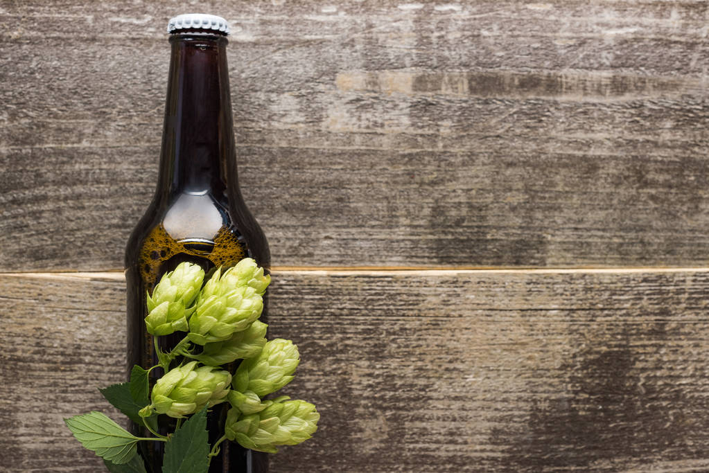 Κορυφαία θέα της φρέσκου μπύρας σε φιάλη με πράσινο άλμα σε ξύλινη επιφάνεια - Φωτογραφία, εικόνα