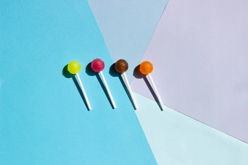 Multi-colored lollipops with hard shadows on an abstract geometric flat background from colored paper. Layout for recording. Flat lay, top view - Photo, Image