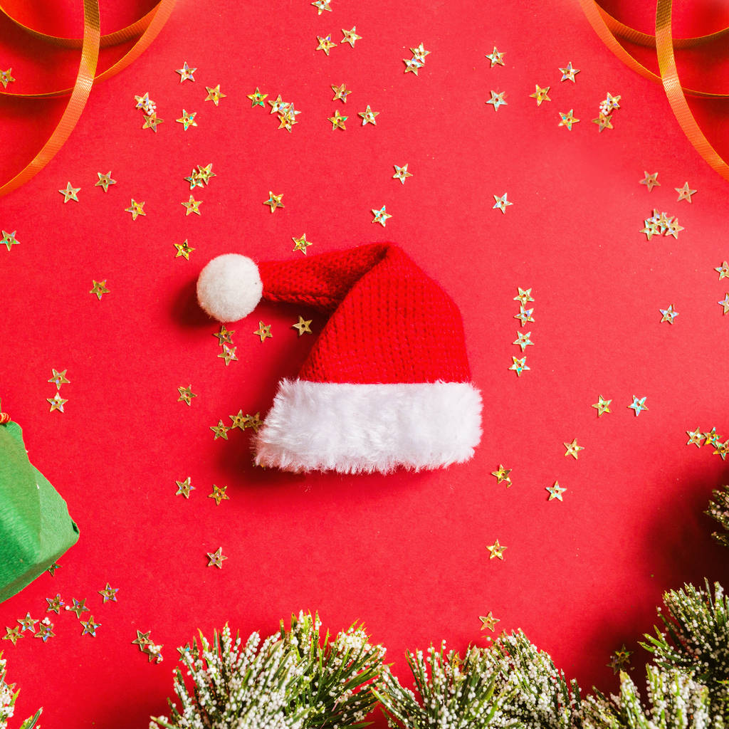 Рождественский подарок, шляпа Санты, подарок, ветки елки на красном фоне с золотыми конфетти. Концепция нового года. Поздравительная открытка, Рождество 2020. Плоская кладка, вид сверху, копировальное пространство, макет
 - Фото, изображение