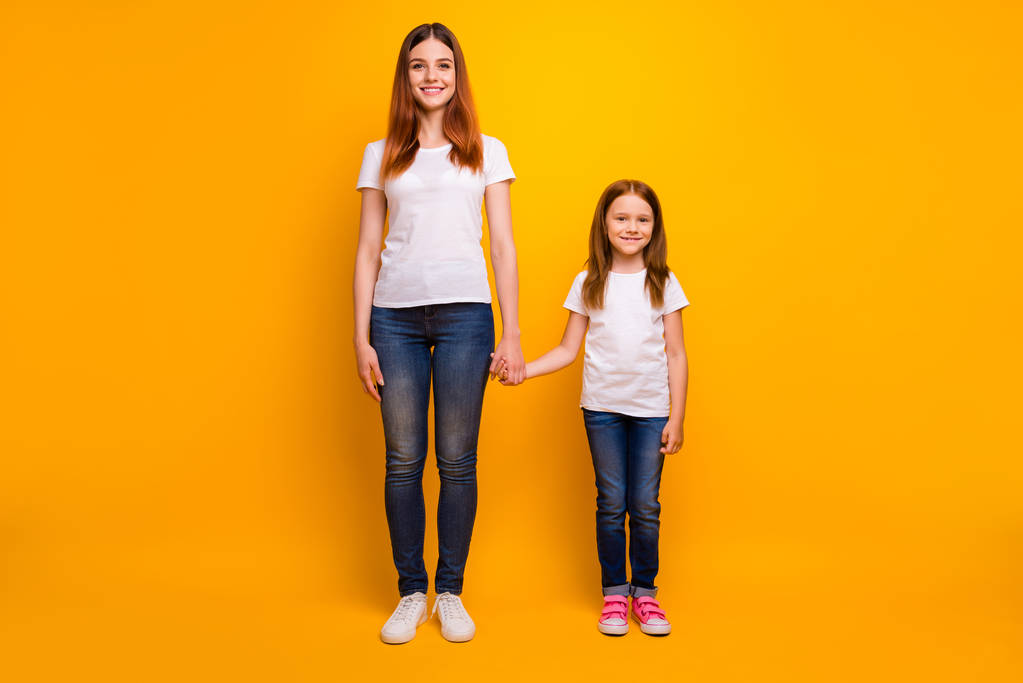 Full size photo of cheerful ladies holding hand smiling wearing white t-shirt denim jeans isolated over yellow background - Photo, Image