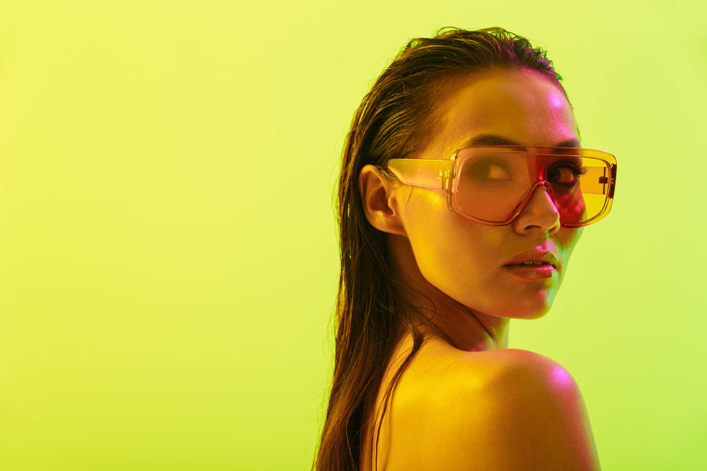 Moda güneş gözlüğü giyen neon parlak ışıklar ile sarı duvar arka plan üzerinde izole poz Amazing genç kadın. - Fotoğraf, Görsel