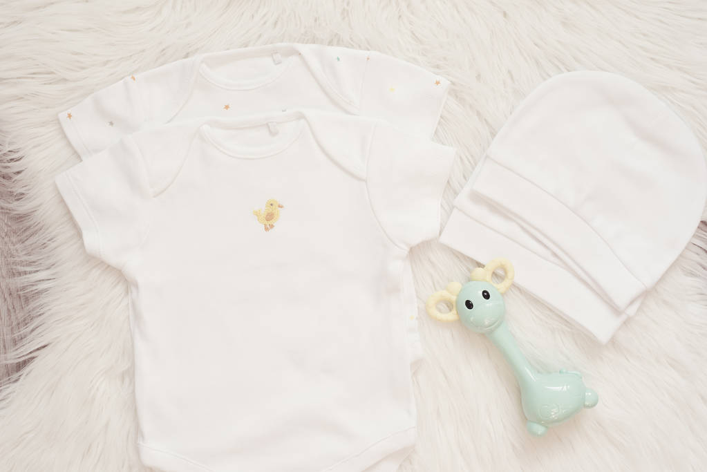 Baby Mockup. Bodysuits, White Hat And Rattle Toy. Baby Jumpsuits, Rompers On A White Fur Carpet. Newborn Concept. Boy or Girls Unisex Clothes - Photo, Image