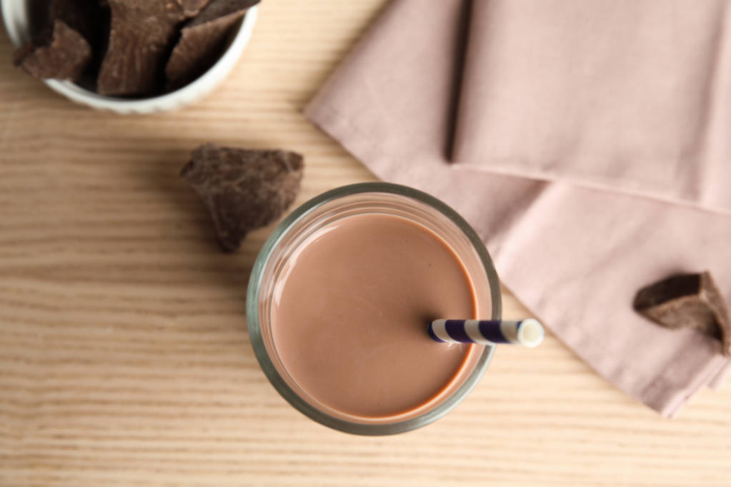Mieszkanie świeckich skład ze szkła o smaczne czekoladowe mleko na podłoże drewniane. Napoje mleczne - Zdjęcie, obraz