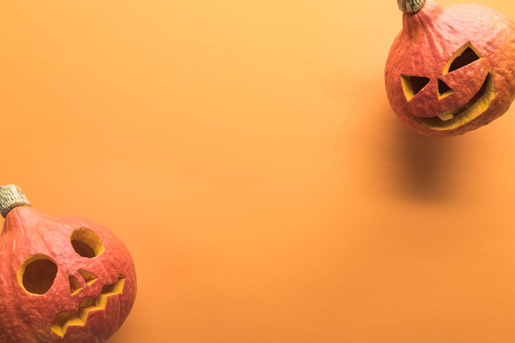 Draufsicht auf geschnitzte gruselige Halloween-Kürbisse auf orangefarbenem Hintergrund mit Kopierraum - Foto, Bild