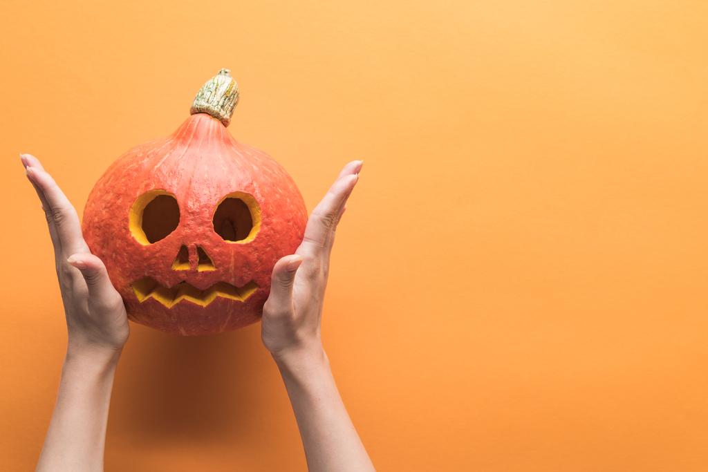 cropped view of woman holding carved spooky Halloween pumpkin on orange background - Photo, Image